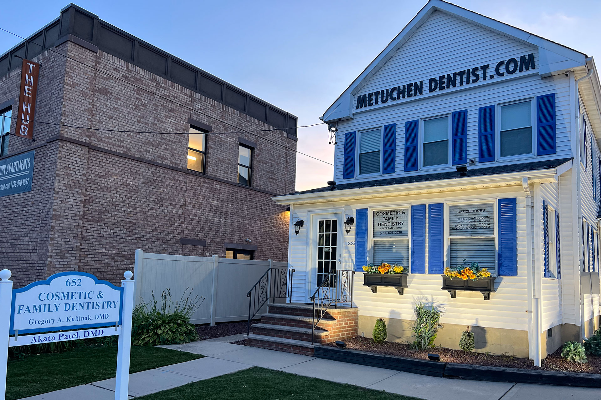 The image shows a sign for a dental practice named Methuen Dentist with a building featuring blue siding and a white sign, set against a night sky with a lit-up house across the street.