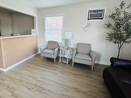 An empty waiting room with a modern design featuring light wood paneling, white walls, a beige carpet, and minimal furniture.