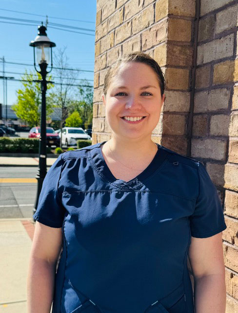 Woman standing outside, smiling at camera, wearing scrubs.